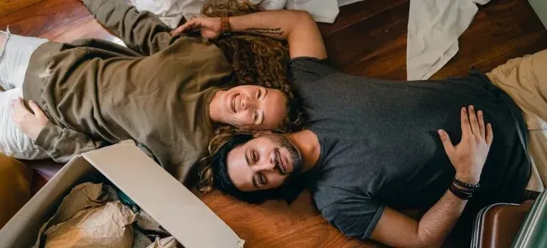 Couple lying on wood floor beside open moving box
