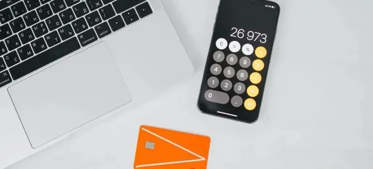 Laptop, phone calculator and orange bank card on desk