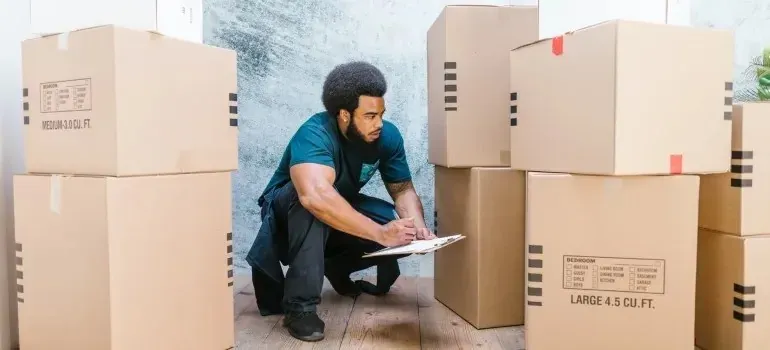 Mover crouching with clipboard checking labeled moving boxes