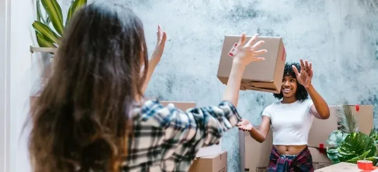 Two women tossing moving box while unpacking together