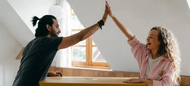 Couple high-fiving over cardboard box in attic room
