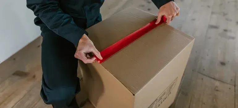 Person sealing cardboard box with red packing tape