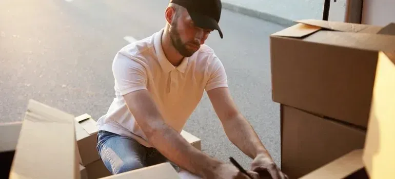Delivery man in plain cap arranging boxes by van