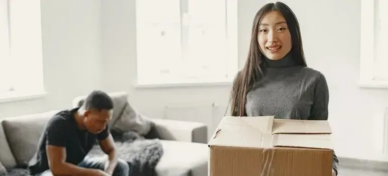 Smiling woman carrying cardboard box in bright living room
