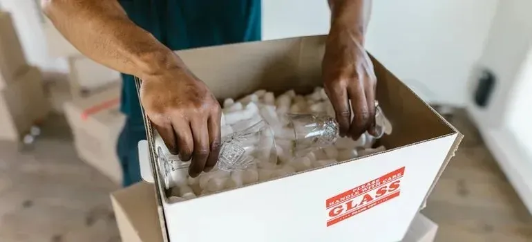 Hands packing glassware into generic glass-marked box with peanuts