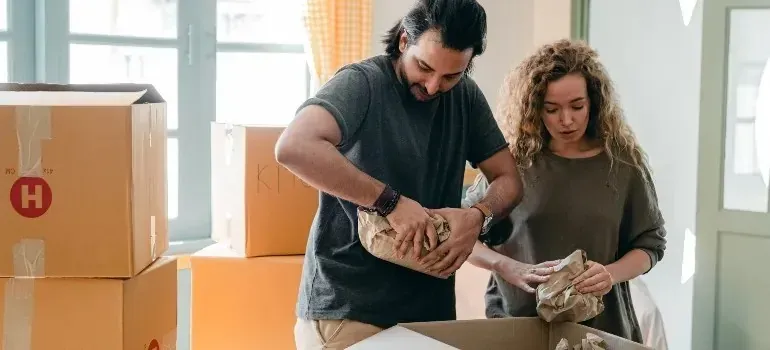 Couple wrapping items in paper beside cardboard moving boxes