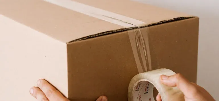 Hands sealing cardboard box with clear packing tape