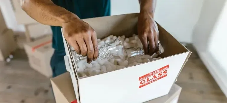 Hands packing glassware into box with generic fragile label