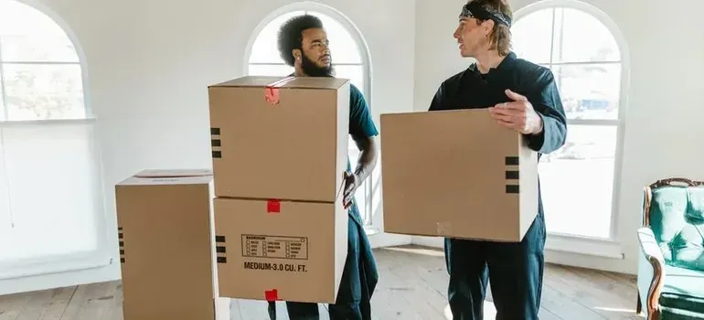 Two movers holding medium cardboard boxes, talking indoors