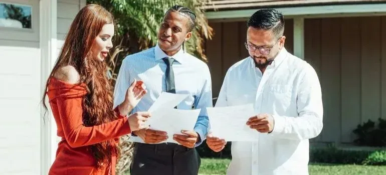 Three people reviewing paperwork outside suburban home