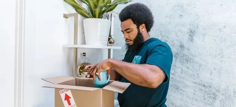 Mover packing blue teapot into caution-labeled cardboard box