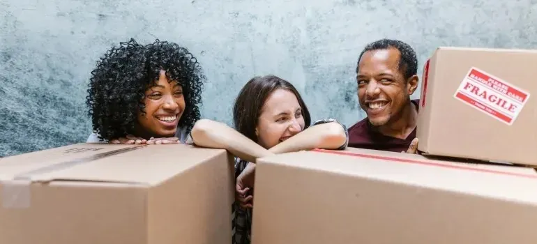 Three happy people peeking over cardboard boxes, fragile sticker