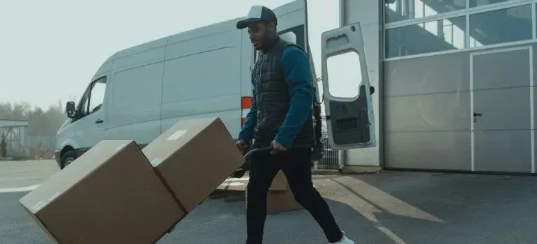 Delivery man wheeling boxes on hand truck by unmarked van
