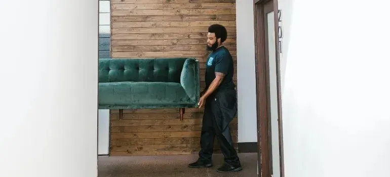 Mover carrying green velvet sofa through office hallway