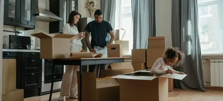 Family unpacking cardboard boxes in kitchen, child drawing