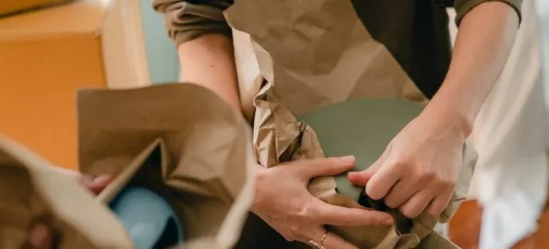 Hands wrapping ceramic bowl in brown packing paper