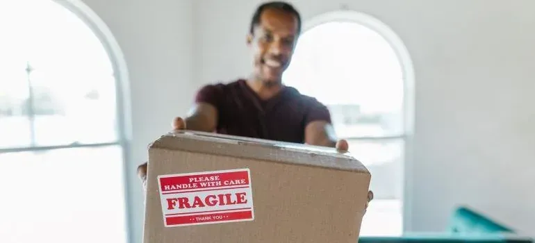 Smiling man handing box with red fragile sticker