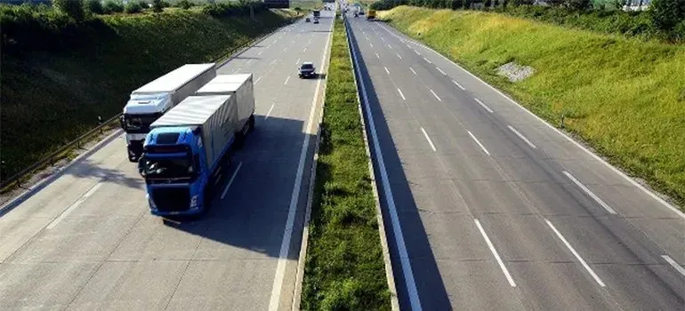 Semi trucks driving on divided highway between green embankments