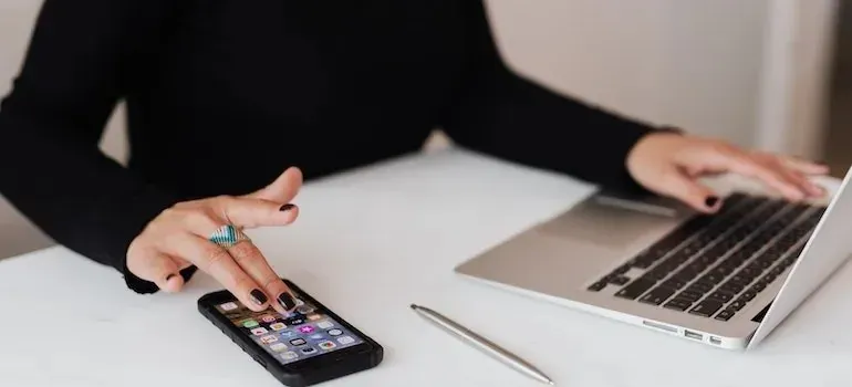 Woman using smartphone and laptop at white desk