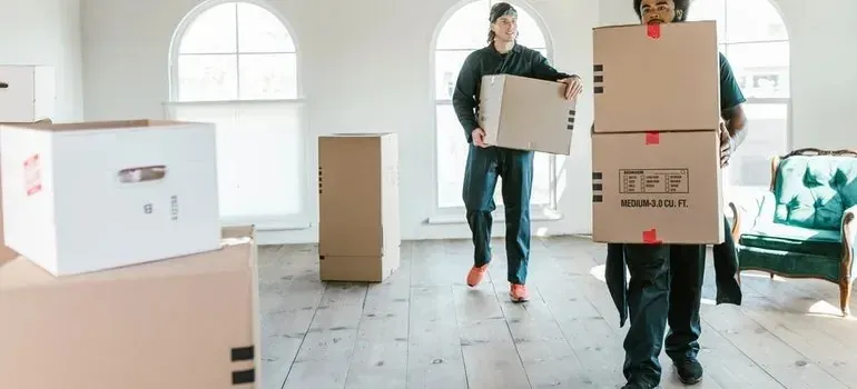 Two movers carrying generic printed moving boxes indoors