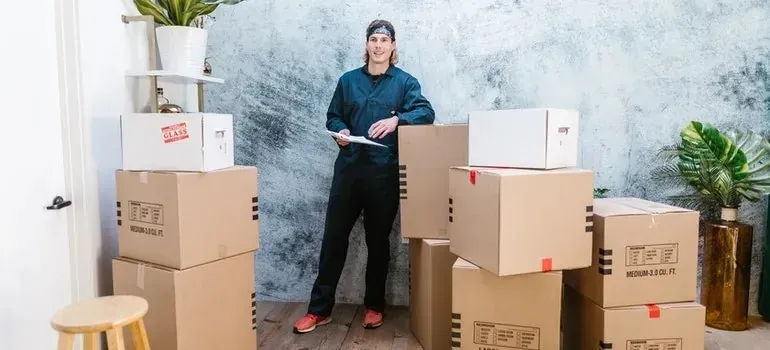 Mover in dark coveralls with clipboard beside stacked boxes