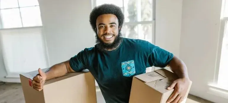 Smiling man carrying two cardboard boxes indoors