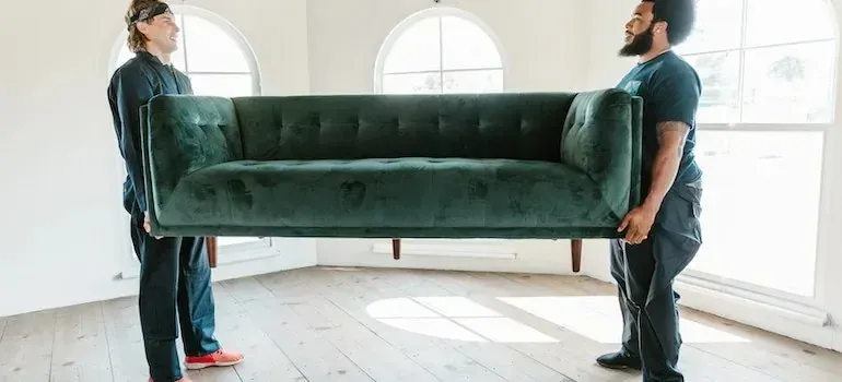 Two movers carrying green velvet sofa in empty room