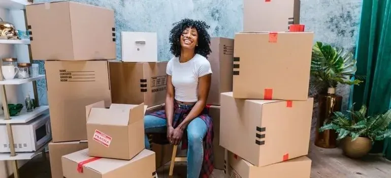 Smiling woman seated among stacked taped moving boxes