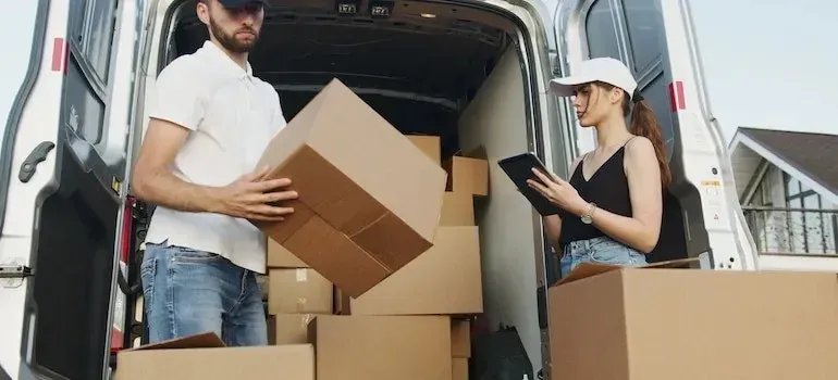 Two movers with tablet unloading boxes from van outside house