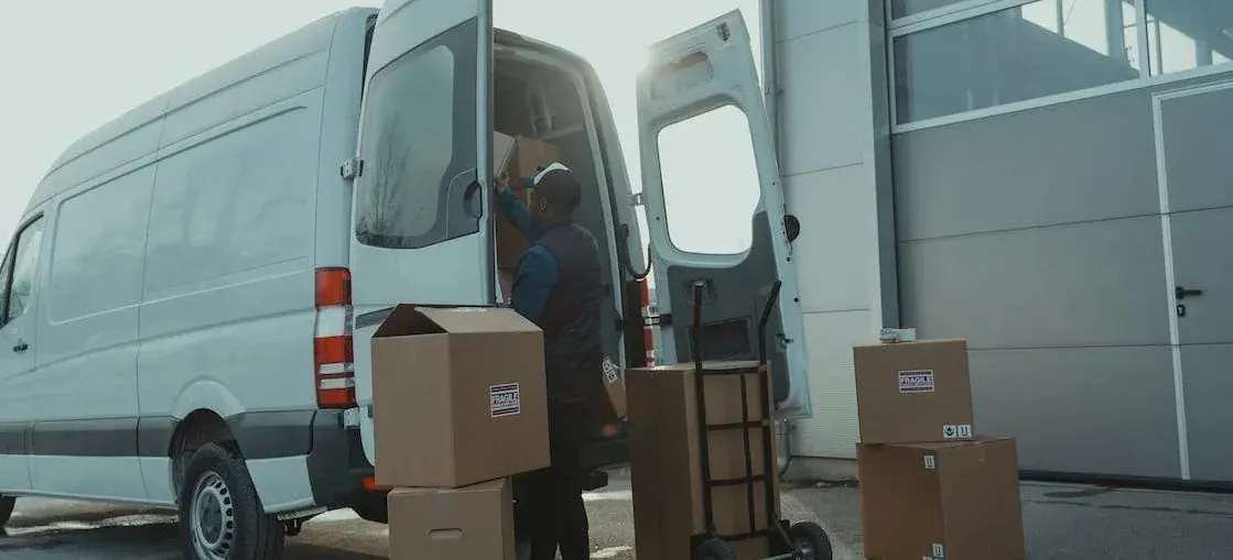 Courier with hand truck loading fragile-labeled boxes into van
