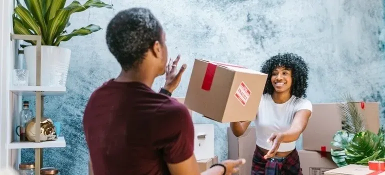 Man tossing fragile-labeled moving box to smiling woman