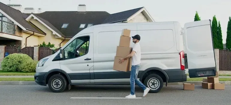 Man loading boxes into unmarked white van outside house
