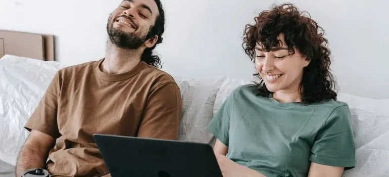 Happy couple sharing laptop among white bedding