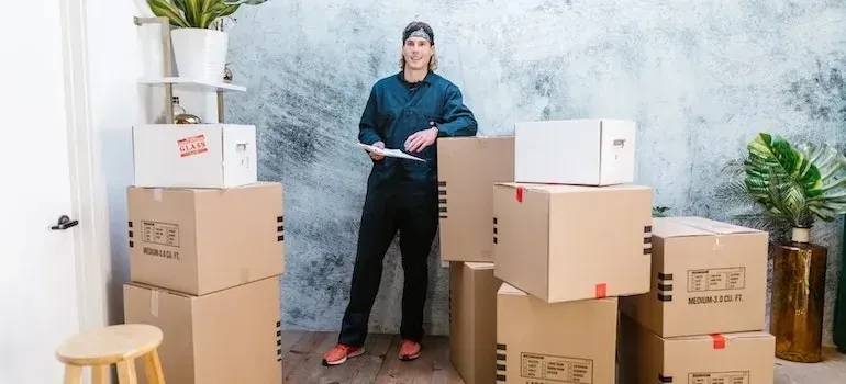 Mover in dark coveralls with clipboard beside stacked boxes