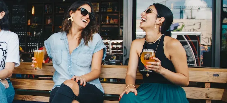 Two women laughing with beers outdoors