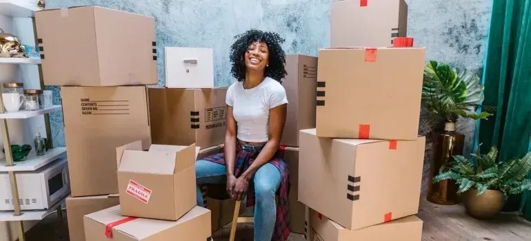 Smiling woman seated among stacked cardboard moving boxes