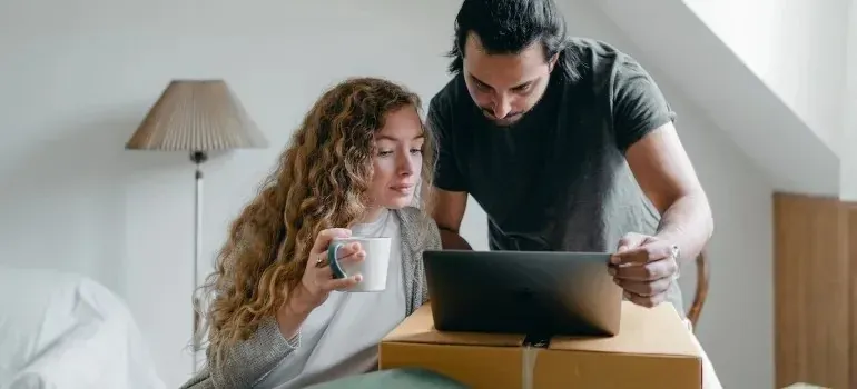 Couple with coffee browsing laptop atop moving box