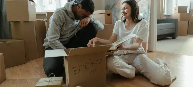 Couple unpacking a cardboard box labeled books at home