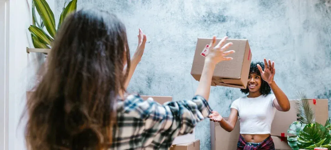 Two women tossing moving box indoors