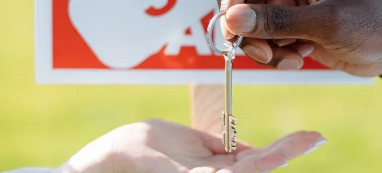 Hand passing house key to open palm, cropped unreadable sign behind