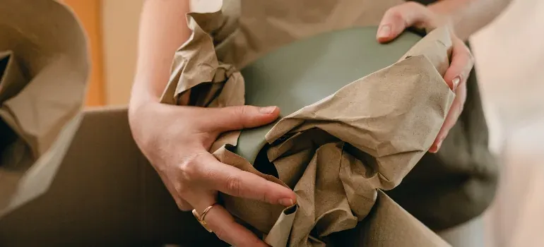 Hands wrapping bowl in kraft paper