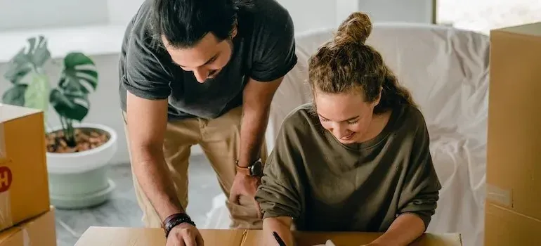 Young couple labeling cardboard box in bright apartment