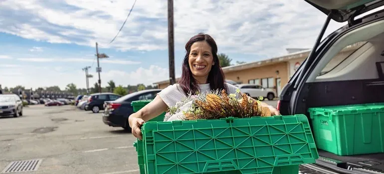 Woman loading green plastic bins into car