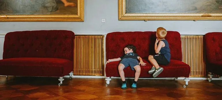Two kids on red sofas in gallery