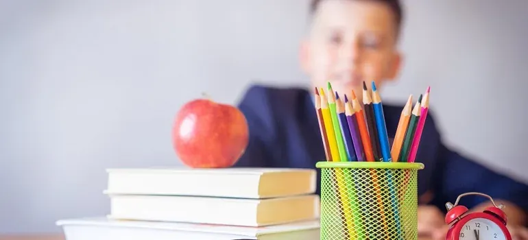 Pencils, books, apple; schoolboy blurred