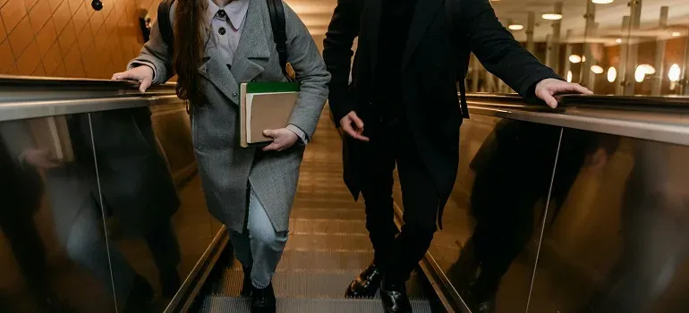 Two people riding escalator with book