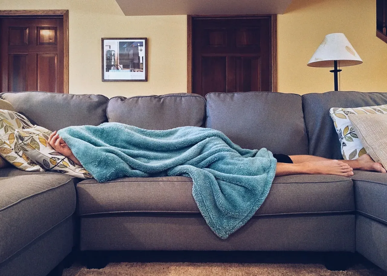 Person napping under blanket on couch